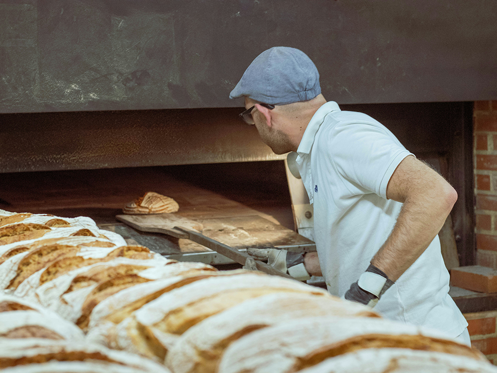 Bäcker backt Brot vor Backofen